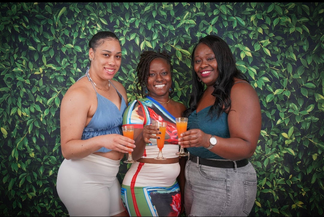 Three women posing together in front of a green leafy background